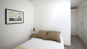A minimalist bedroom with a bed, a framed picture on the wall, and a bedside table with a lamp.
