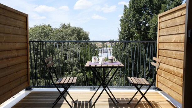 A wooden deck with a table and two chairs, overlooking a scenic view of trees and buildings.