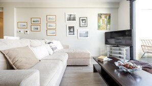 Ett modernt vardagsrum med en beige soffa, en platt-TV på ett vitt TV-bord och en glasskål på ett mörkt träbord.