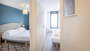 Ett sovrum med en säng, ett nattduksbord, en lampa, ett fönster och en dörr som leder till ett annat rum.