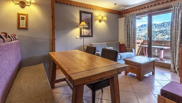 Una stanza accogliente con un tavolo di legno, un divano e un balcone con vista sulle montagne.