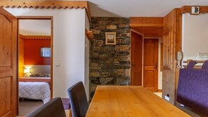 Un tavolo da pranzo in legno con sedie, un muro in pietra e un letto con una parete rossa sullo sfondo.