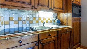 Una cucina con mobili in legno, zoccolo in piastrelle, lavello e forno a microonde.