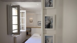 Een slaapkamer met een bed, nachtkastje, wandplank en raam met open deur.