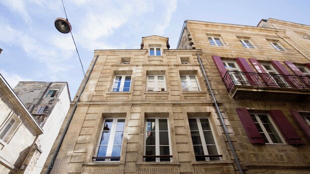 Een meerhoog gebouw in klassieke bouwstijl, met een centrale ingang met een topgevel, meerdere ramen met luiken en een zichtbaar balkon aan de rechterzijde.
