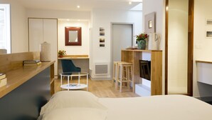 A modern hotel room with a wooden desk, a comfortable bed, a small round table, and a seating area with a chair and stools. - Bordeaux Historic Center Superior double studio (Burdeos)