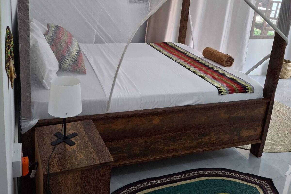 A bed with a mosquito net, a bedside table with a lamp, and a woven rug.