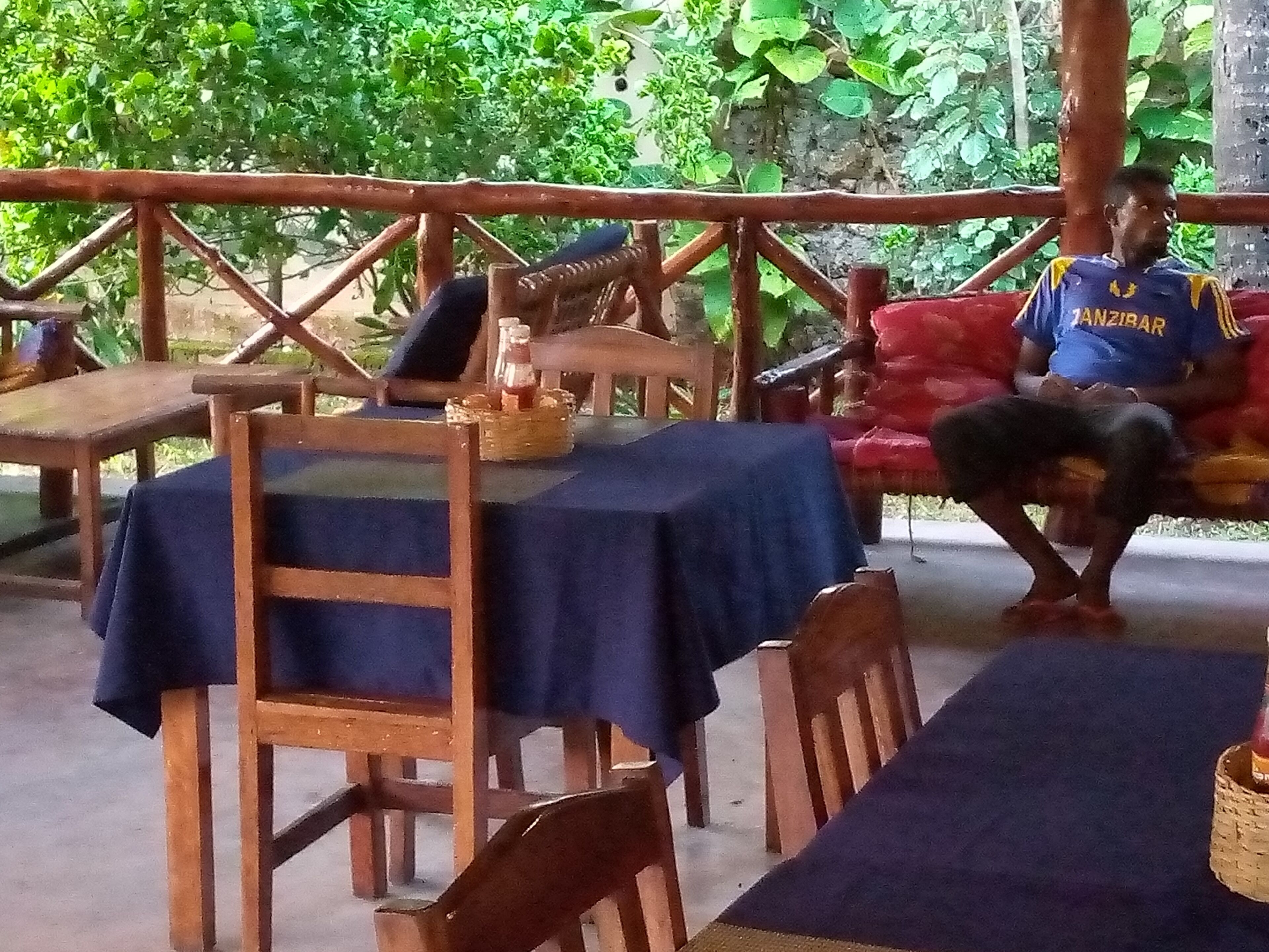 Un área de estar al aire libre con mesas y sillas de madera, cubiertas con manteles azules.