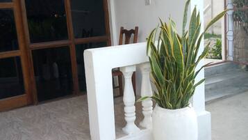 A white bench with a potted plant beside it, a wooden chair, and a window with decorative bars.
