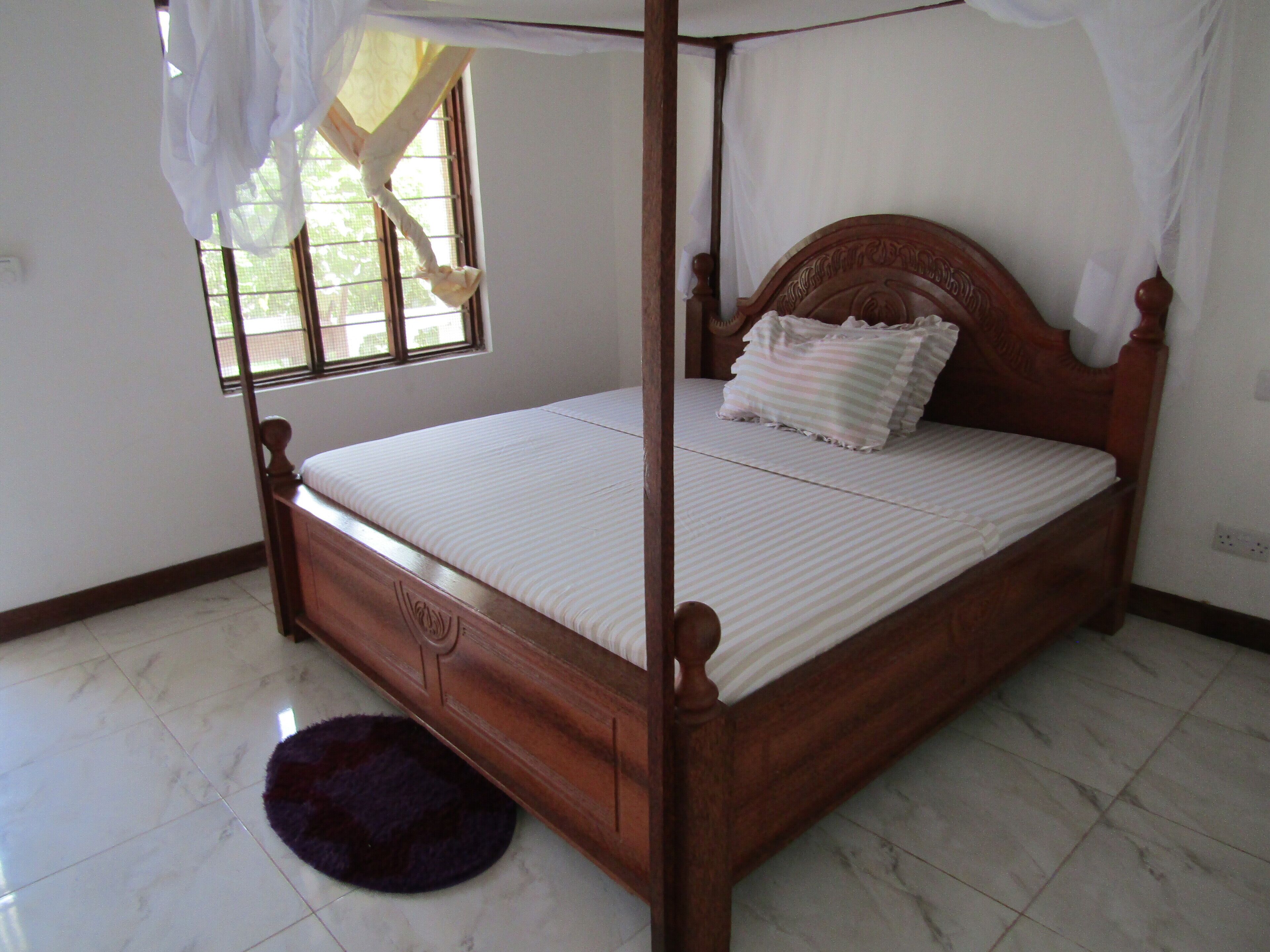 Una cama con dosel y tablero de madera, colchón blanco y almohada a rayas.