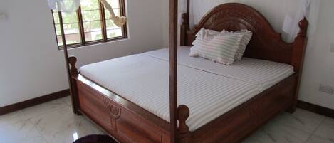 A four-poster bed with a wooden headboard, a white mattress, and a striped pillow.