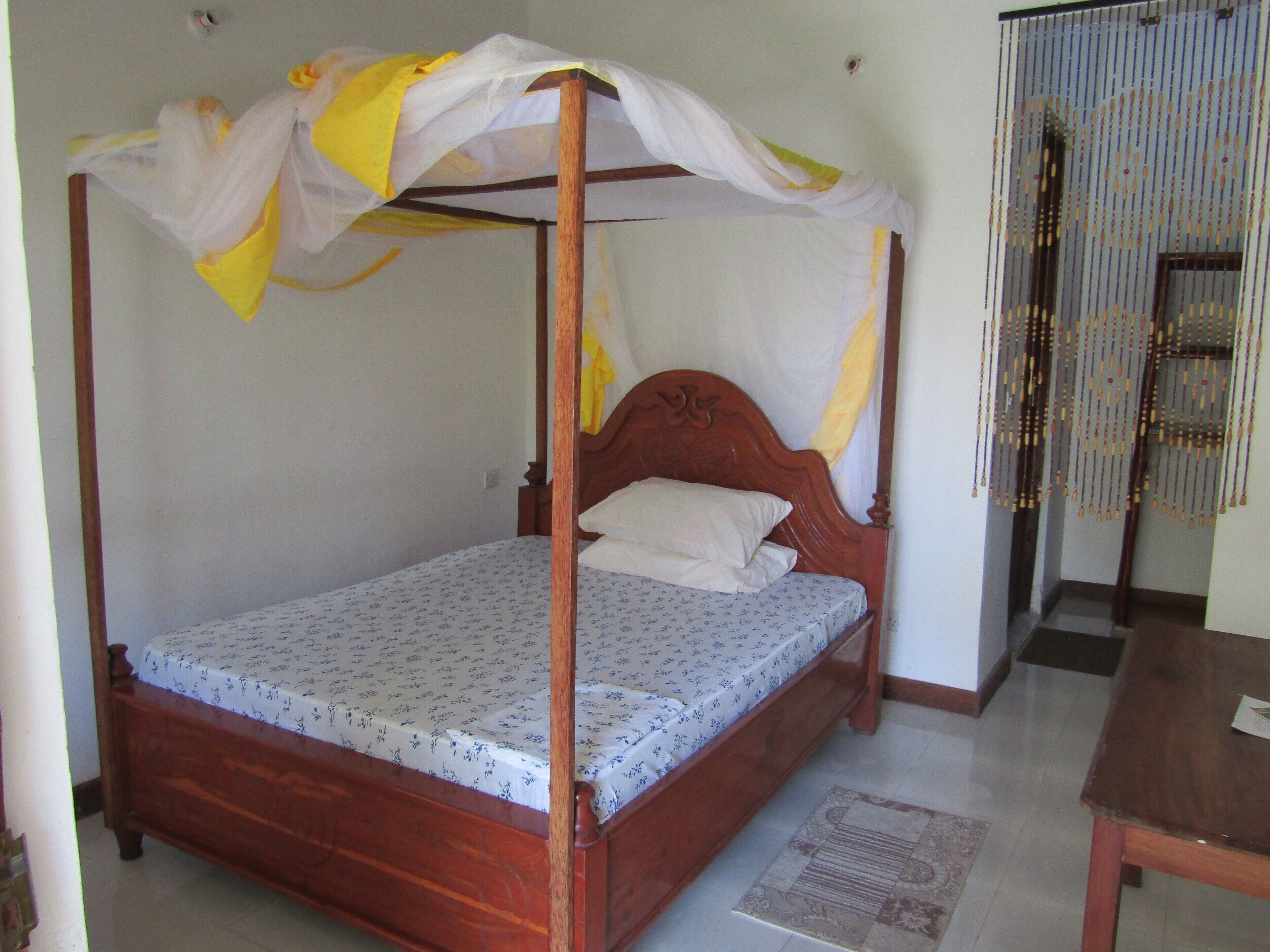 Una cama con dosel, con doselres de tela amarilla y blanca, ropa de cama floral y un cabecero de madera.
