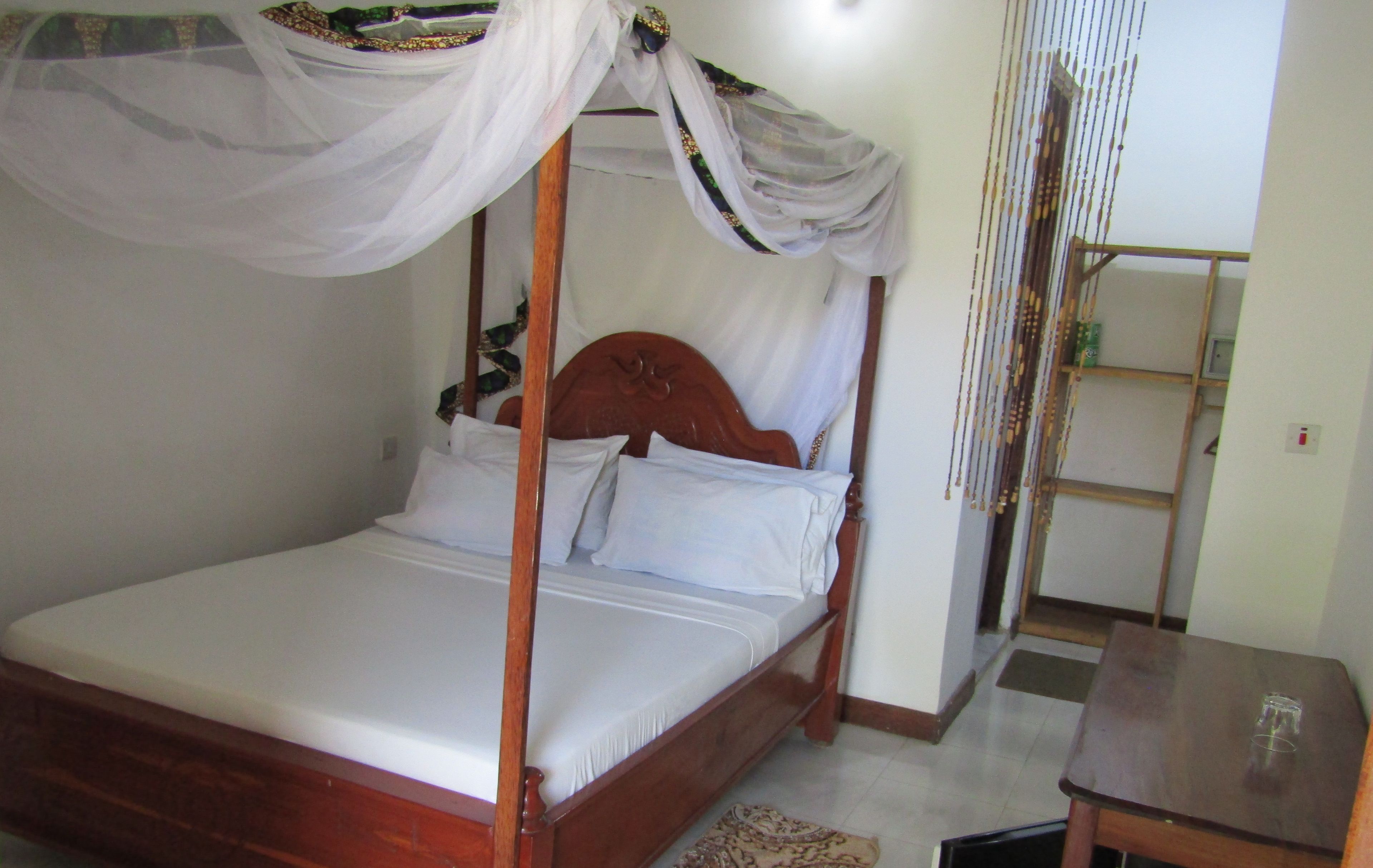 A four-poster bed with a canopy, a wooden headboard, and a bedside table with a glass.