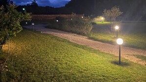 A nighttime outdoor scene with a gravel path, illuminated by street lamps, surrounded by grass and trees. - Exclusive Farm (S'arena Scoada)