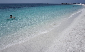 A beach with clear turquoise water, a sandy shore, and a person swimming. - Exclusive Farm (S'arena Scoada)