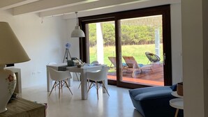 A modern living room with a dining area, large sliding glass doors to a patio, and a view of a green landscape. - Exclusive Farm (S'arena Scoada)