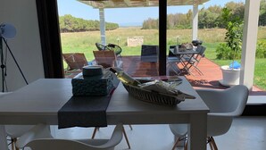 A modern dining area with a table set for two, a large window offering a view of the outdoors, and a pergola structure. - Exclusive Farm (S'arena Scoada)