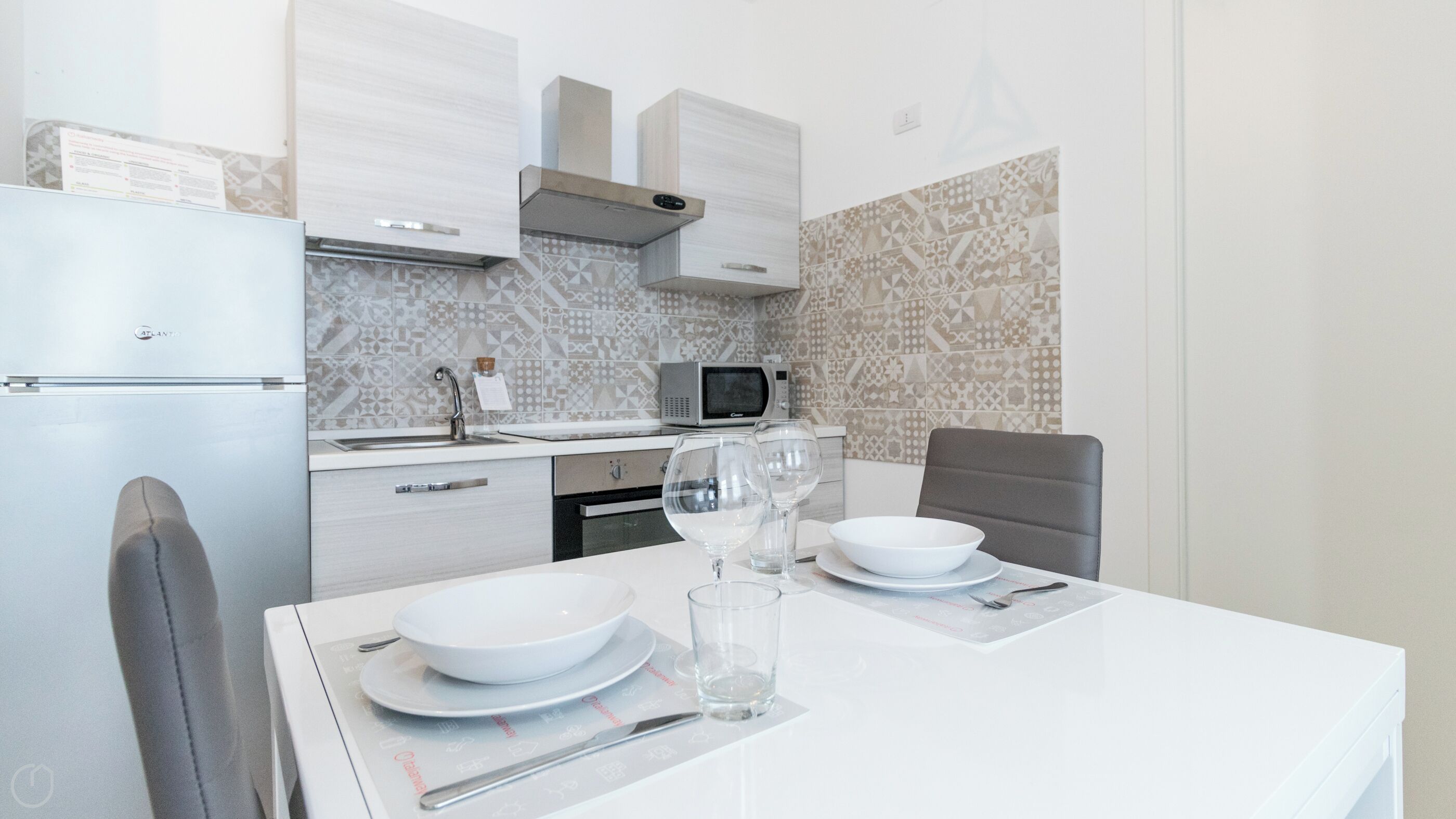 A modern kitchen with white cabinets, a microwave, and a sink. There is a dining table with plates, glasses, and cutlery.