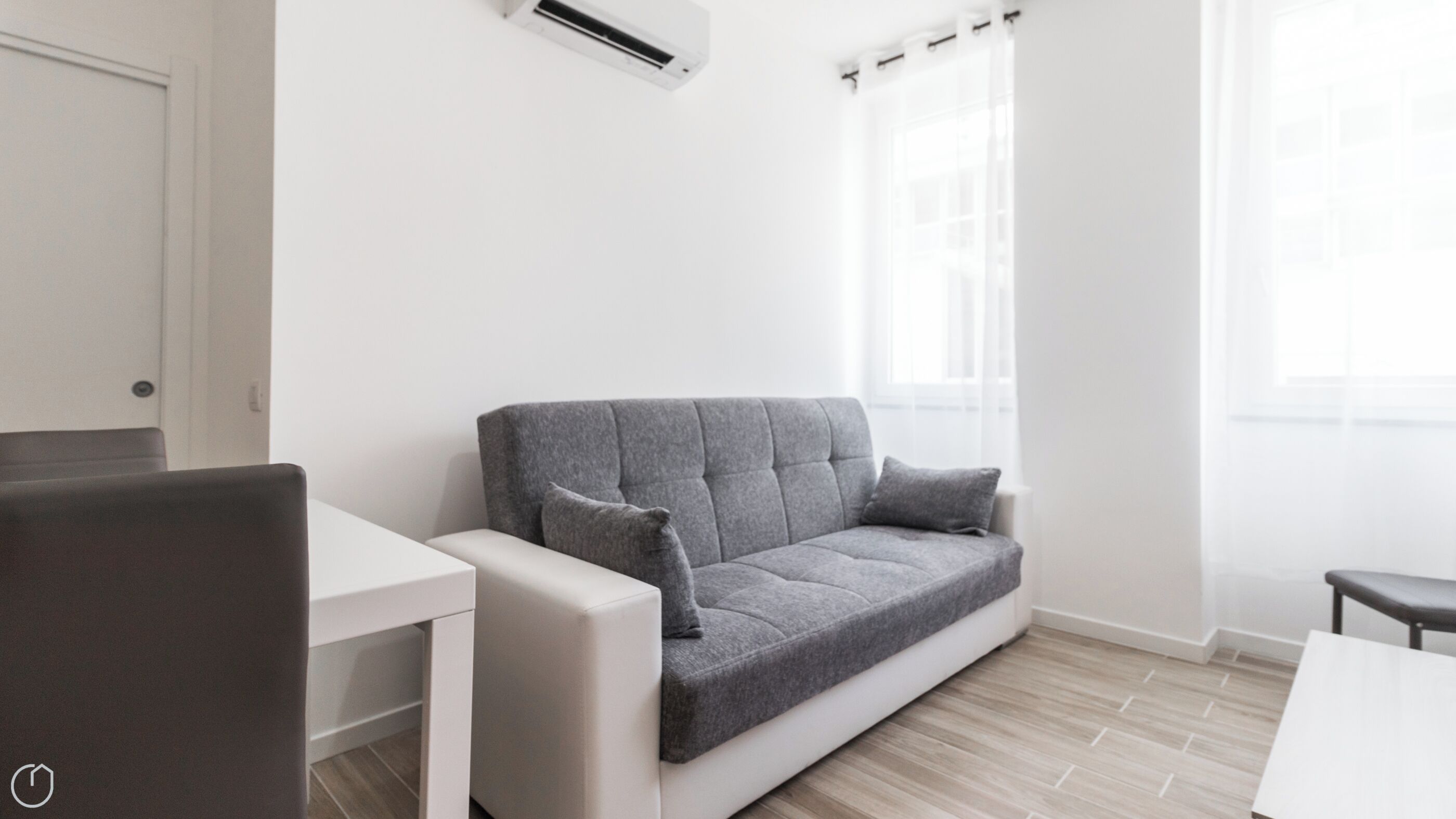 A modern living room with a grey sofa, a white table, and a window with sheer curtains.