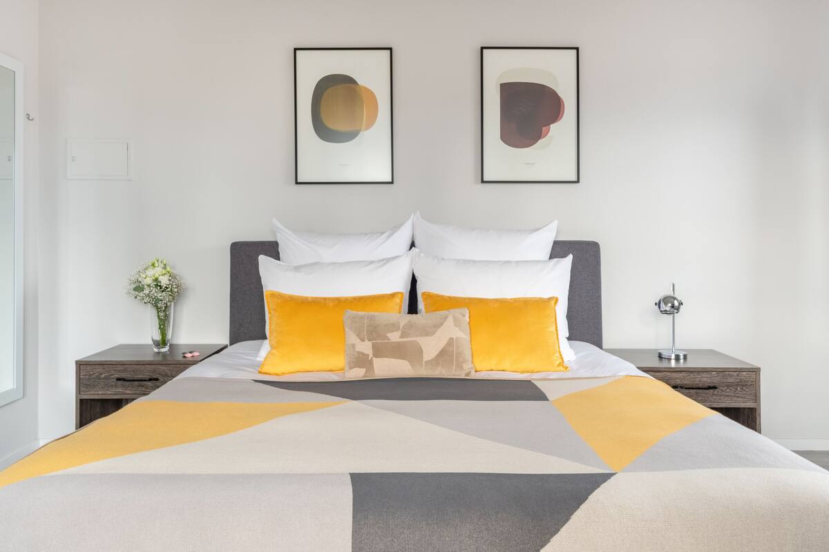 Une chambre à coucher moderne avec un grand lit, deux tables de chevet et des œuvres d’art accrochées au mur.