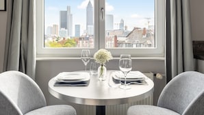 Una mesa de comedor con platos, vasos y un jarrón de flores, con vistas a la ciudad a través de amplios ventanales.