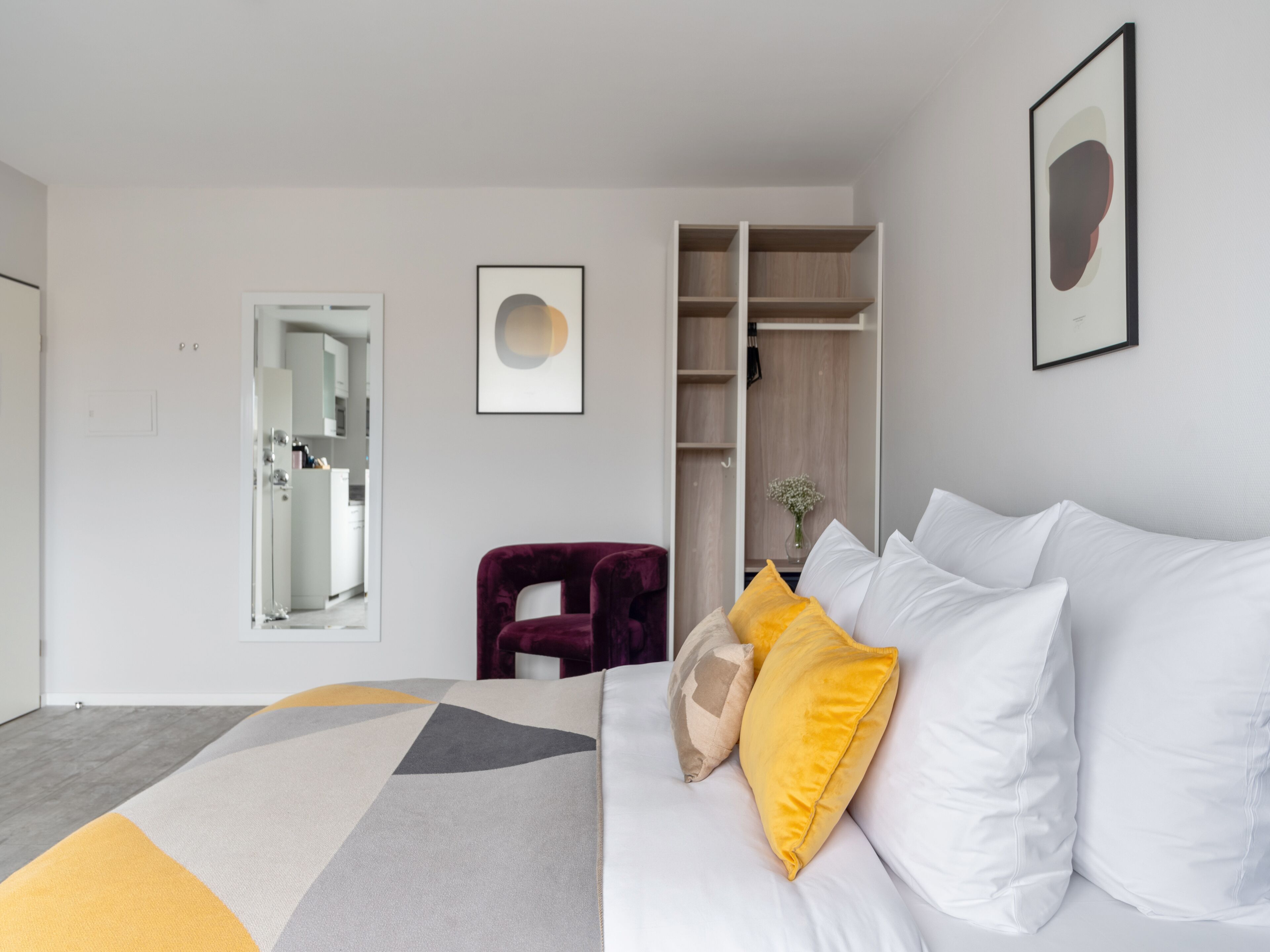 A modern hotel room with a bed, a wardrobe, a mirror, and a framed picture on the wall.