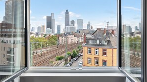 Un paisaje urbano a través de una ventana, con varias vías de tren y una mezcla de edificios modernos y tradicionales.