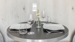 A round dining table with two white plates, two wine glasses, a vase with a flower, and a water glass. - Numa Frankfurt Blau (Frankfurt)