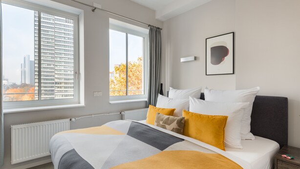 A modern hotel room with a large bed, two windows, a radiator, and a framed picture on the wall. - Numa Frankfurt Blau (Frankfurt)