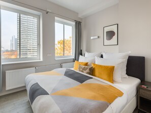 A modern hotel room with a large bed, two windows, a radiator, and a framed picture on the wall. - Numa Frankfurt Blau (Frankfurt)