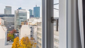 A cityscape through a window with a view of modern buildings and a tree with yellow leaves. - Numa Frankfurt Blau (Frankfurt)