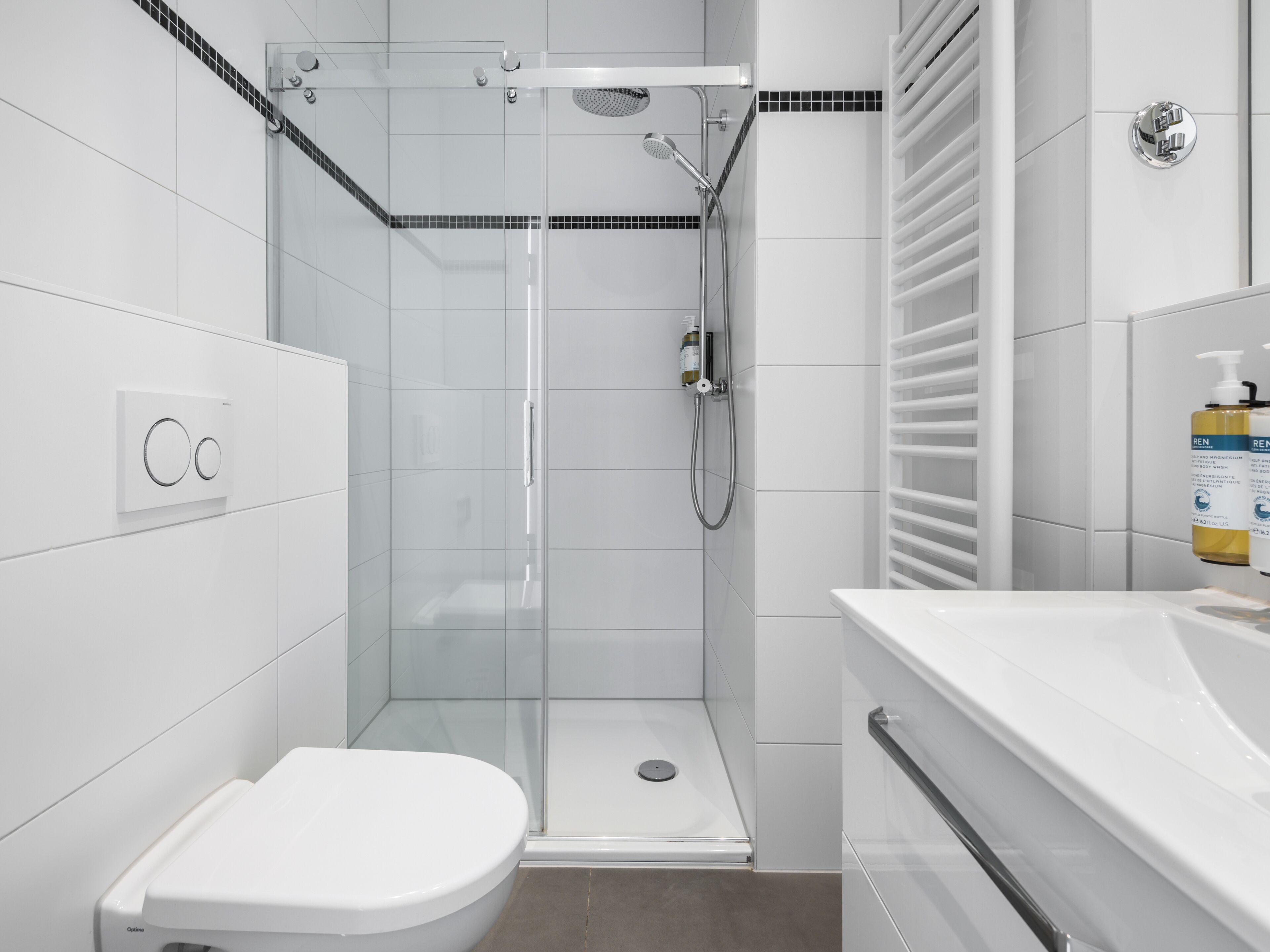 Un baño moderno con ducha envuelta en vidrio, inodoro blanco y tocador con espejo.