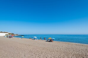 A beach with umbrellas, people, and a clear blue sky.