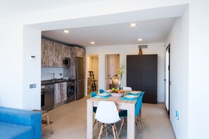 A modern kitchen with a microwave, dishwasher, and wooden cabinets. There is a dining area with a table set for four, chairs, and a vase with flowers.