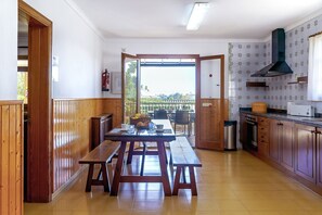 Une cuisine avec des meubles en bois, un coin repas avec une table et des bancs, et une vue sur une terrasse extérieure.