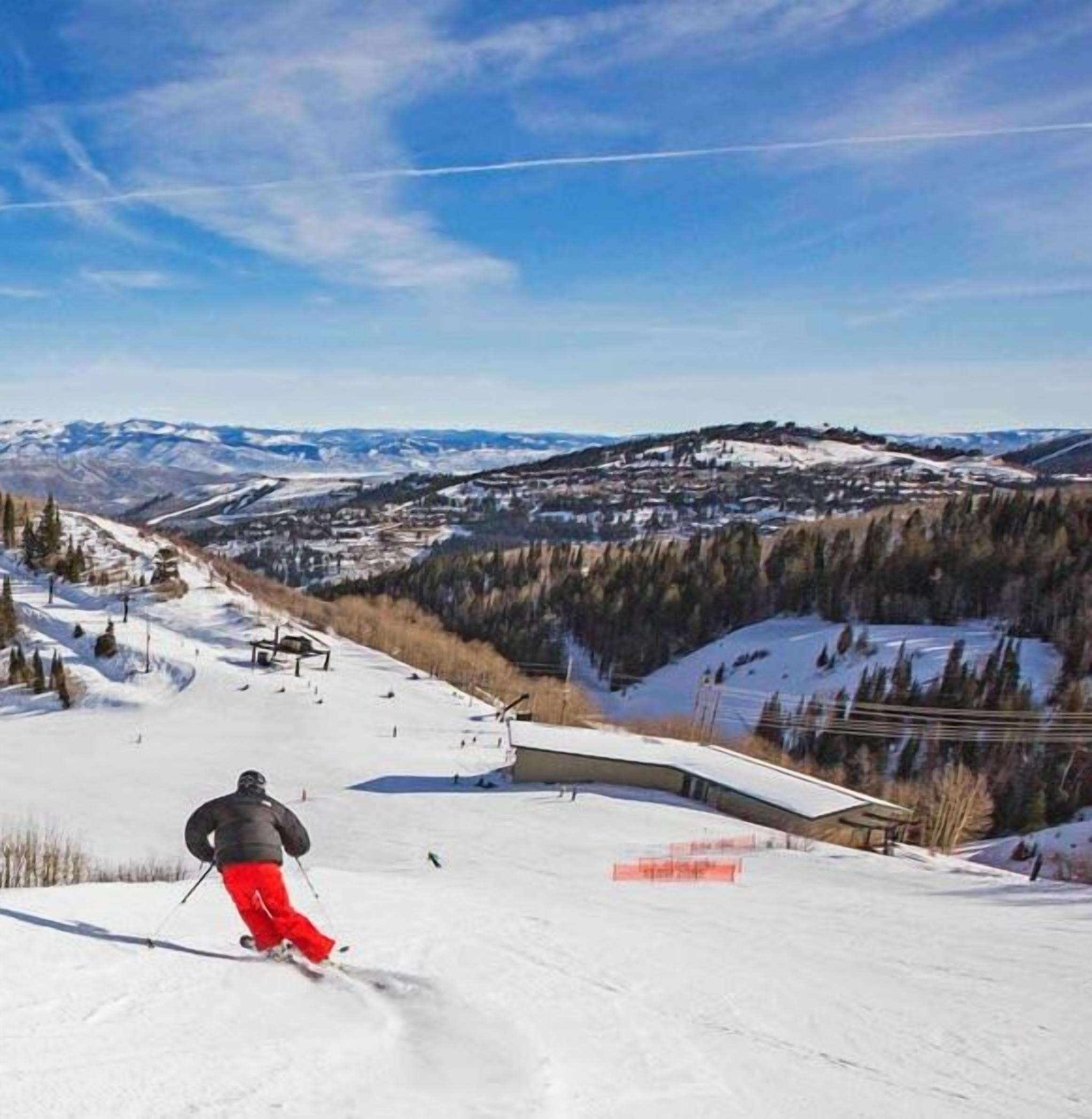 Een skipiste met een skiënde persoon, een stoeltjeslift en een besneeuwd berglandschap op de achtergrond.