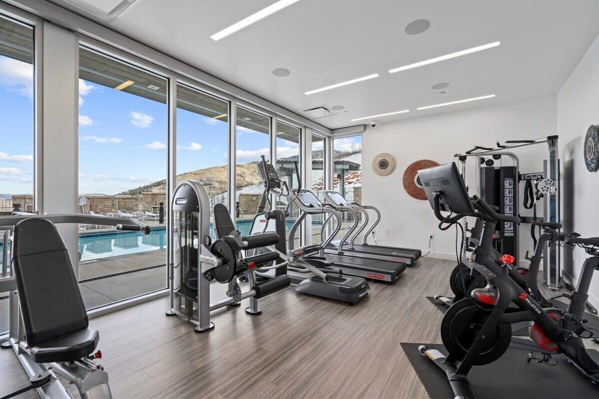 A gym with cardio machines, weightlifting equipment, and a view of a swimming pool.