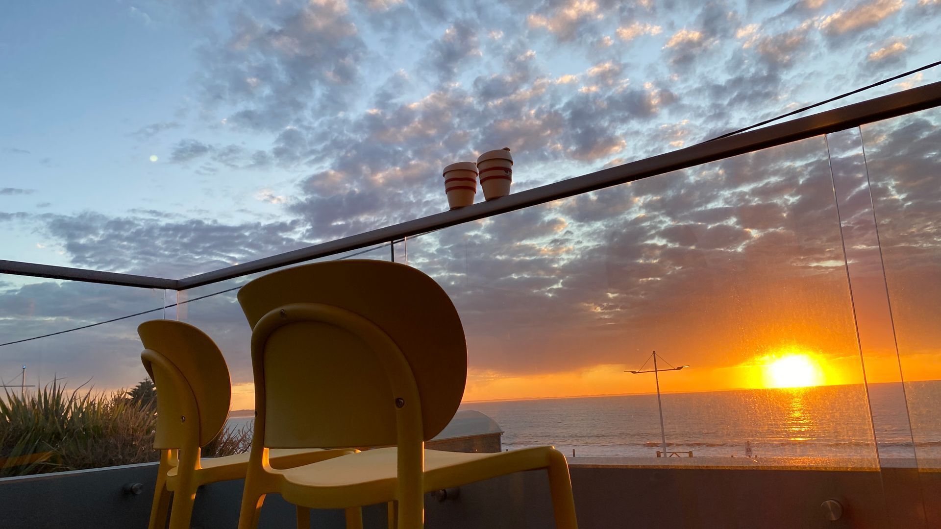 A balcony with yellow chairs and a railing overlooking the sea during sunset.
