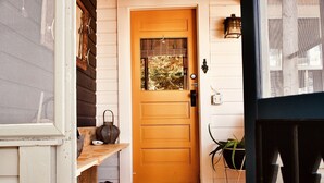A wooden door with a window, a small bench, a potted plant, and a wall-mounted light fixture. - Woodhaven Hideaway on Woods Pond.. (Bridgton)