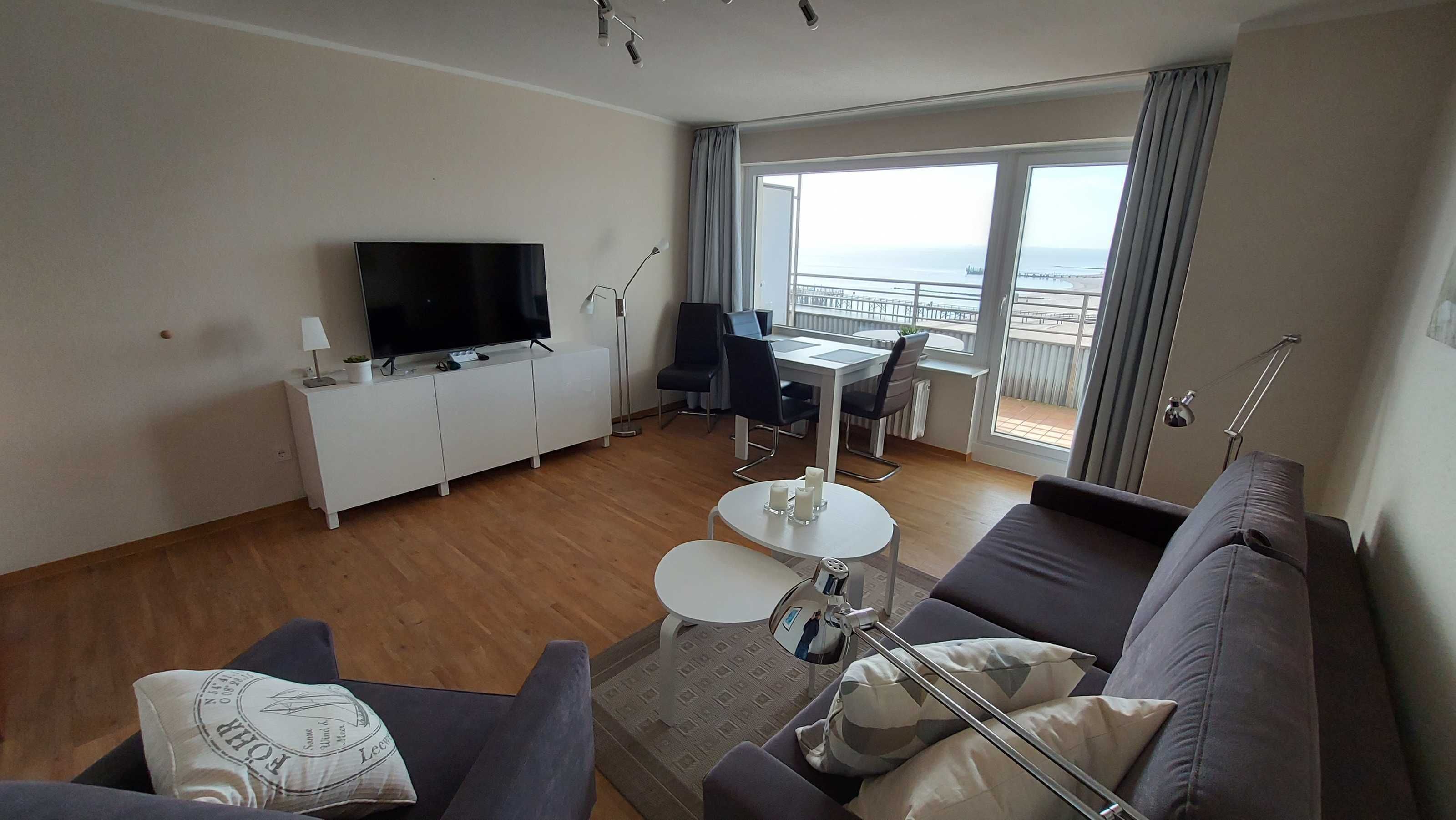Una sala de estar moderna con un televisor de pantalla plana, un sofá, una mesa de comedor y un balcón con vistas.