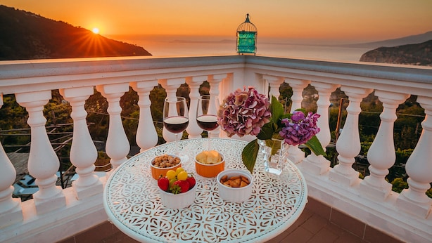Un balcón con una mesa dispuesta para una comida, con vistas a un hermoso atardecer.