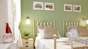 Un dormitorio con dos camas, una mesita de noche con lámpara, una planta en maceta y una pared decorada con cuadros.