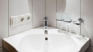 Un lavabo blanc pour la salle de bain, doté d’un robinet chromé, de deux prises électriques et d’un porte-savon en verre.