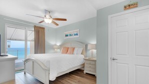 A bedroom with a bed, bedside tables, a ceiling fan, and a view of the ocean through a sliding door.