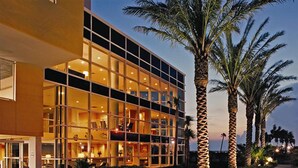 A modern hotel with a glass facade, multiple floors, and a palm tree-lined entrance.