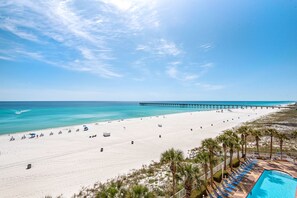 Ein Strandresort mit einer langen Pier, die ins Meer führt, einem Sandstrand und einem Poolbereich mit Liegestühlen.