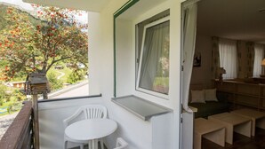 Un balcon avec une table et des chaises, une fenêtre avec des rideaux et une vue sur un arbre et des montagnes.