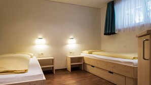 Ein kleiner, gut beleuchteter Raum mit zwei Betten, einem Nachttisch und einem Holzschrank.