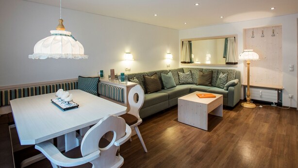Ein modernes Wohnzimmer mit Essbereich, einem grünen Sofa, einem weißen Tisch und einer Hängeleuchte.