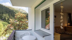 Ein Balkon mit Tisch und Stühlen, einer Sitzecke und Blick auf einen bewaldeten Berg.